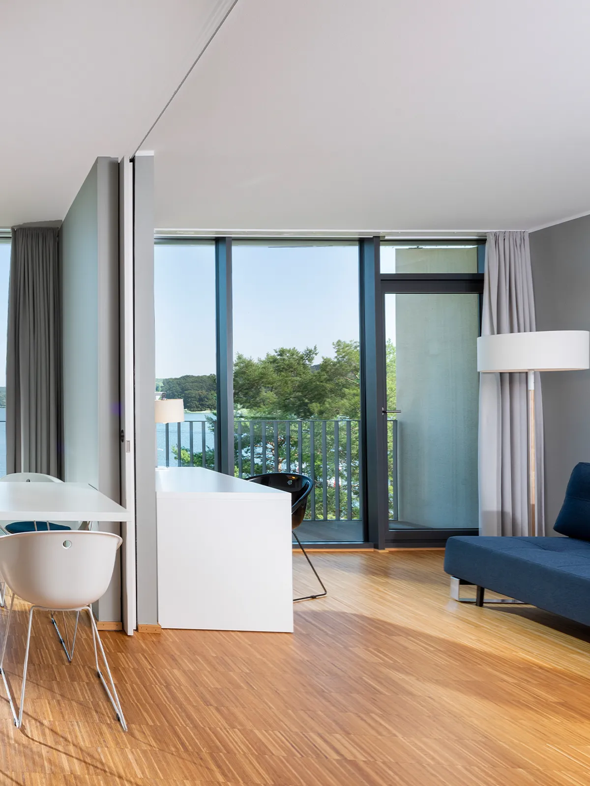 Eleganter Wohnbereich im Panorama-Apartment des Waveboard Hotels Potsdam mit stilvollem Sofa, modernem Schreibtisch und bodentiefen Fenstern. Helle, offene Raumgestaltung mit Blick auf die Havel.