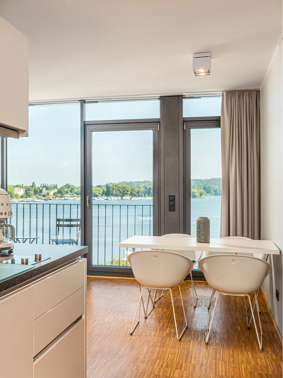 Moderner Essbereich im Seeblick-Apartment des Waveboard Hotels Potsdam mit stilvollen Möbeln, offener Küche und bodentiefen Fenstern. Traumhafter Blick auf die Havel für ein einzigartiges Wohnerlebnis.