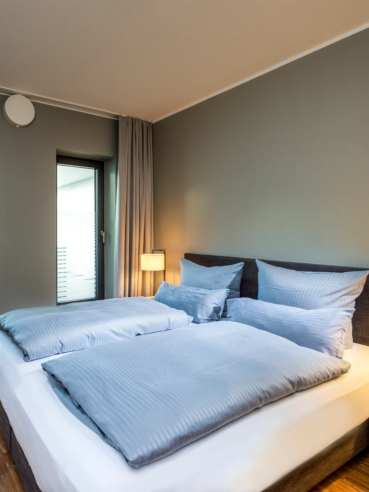Gemütlicher Schlafbereich im Zwei-Zimmer-Apartment des Waveboard Hotels Potsdam mit komfortablem Doppelbett und stilvoller Beleuchtung. Die sanften Farbtöne und hochwertige Bettwäsche sorgen für eine entspannte Atmosphäre.