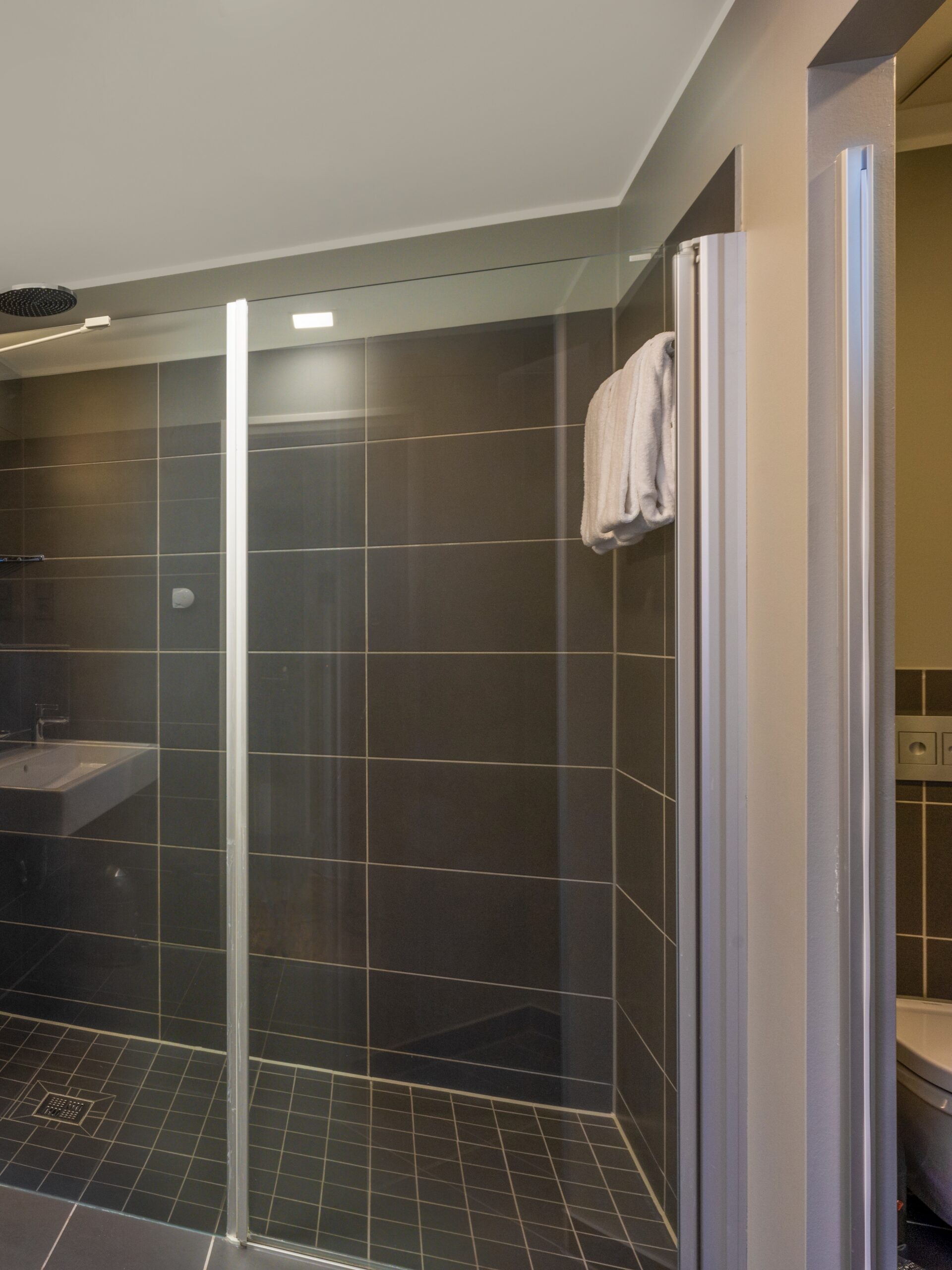 Modernes Hotelbad im Wavehotel Potsdam mit großer begehbarer Dusche und dunklen Fliesen