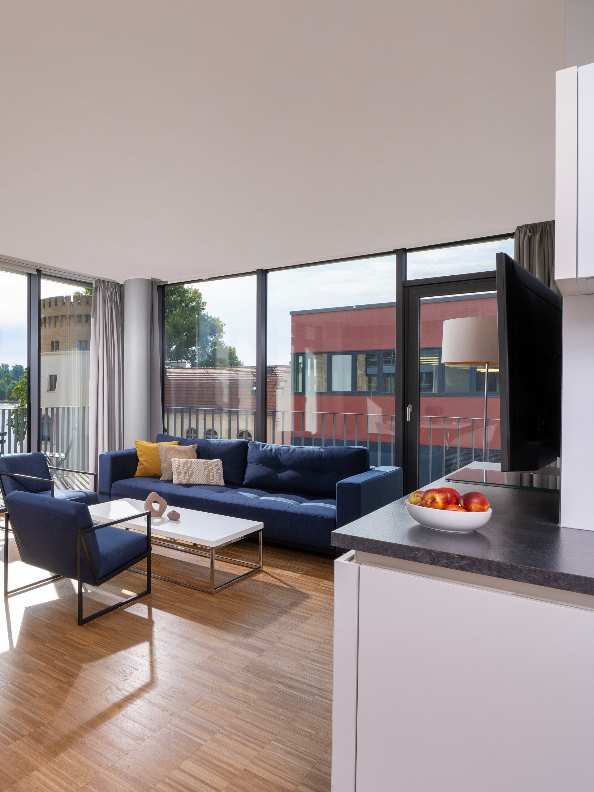 Modernes Wohnzimmer im Wavehotel Potsdam mit großen Fenstern, blauem Sofa und hellen Holzboden