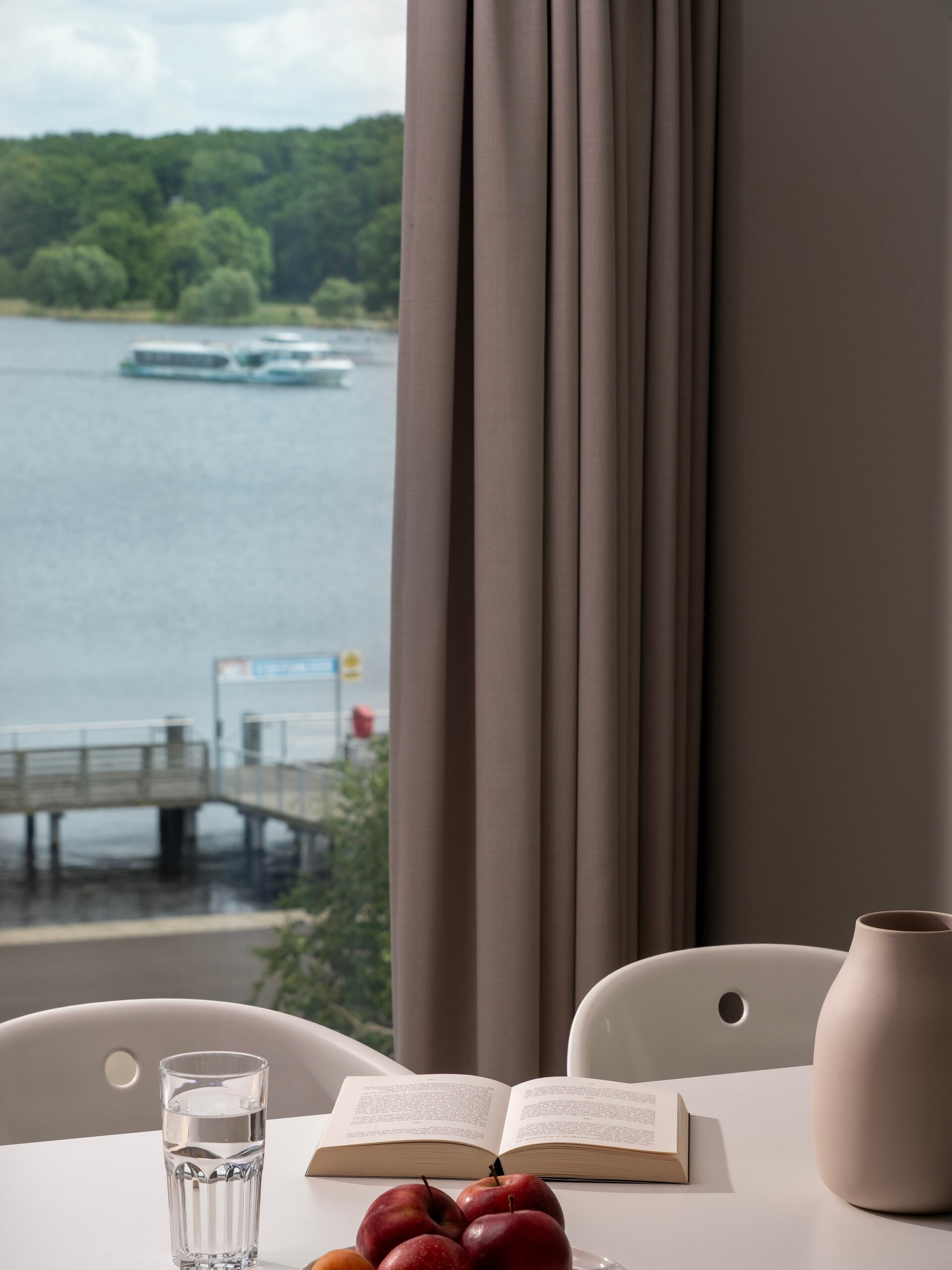 Apartment im Wavehotel Potsdam mit Blick auf die Havel, gedecktem Tisch mit Äpfeln, Buch und Glas Wasser