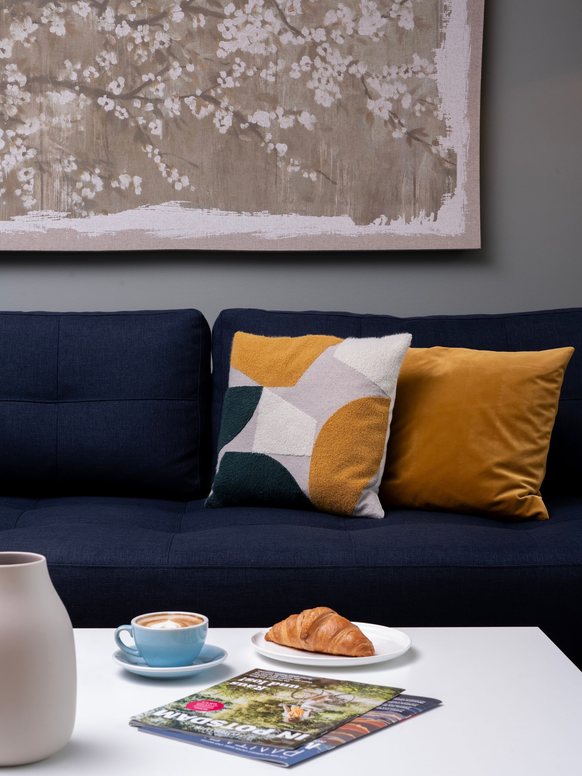 Gemütlicher Wohnbereich im Wavehotel Potsdam mit dunkelblauem Sofa, Design-Kissen, Kaffee und Croissant auf dem Tisch