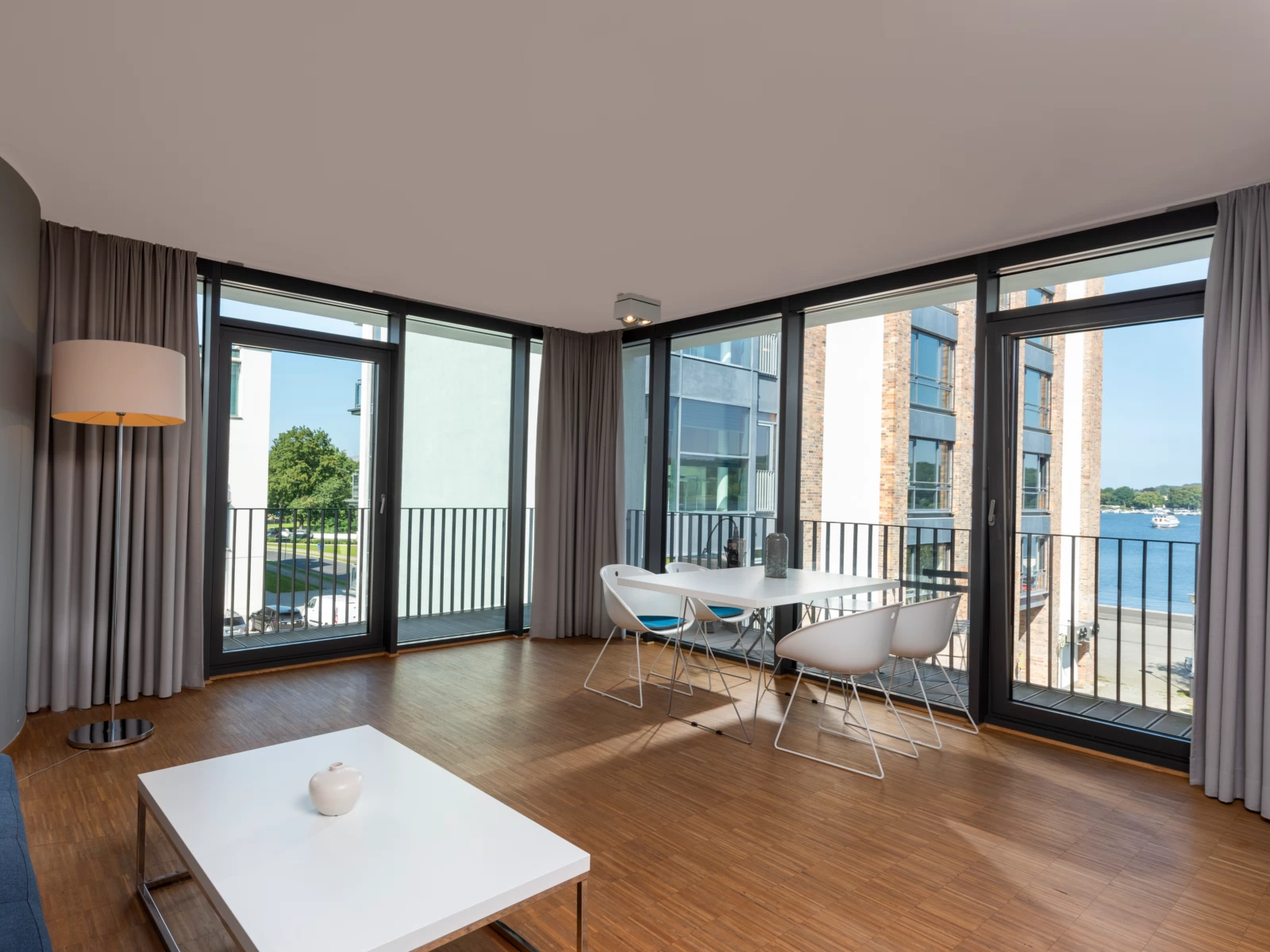 Heller Essbereich im Zwei-Zimmer-Apartment des Waveboard Hotels Potsdam mit modernem Design und bodentiefen Fenstern. Der angrenzende Balkon bietet einen malerischen Blick auf den Templiner See und sorgt für eine entspannte Atmosphäre.
